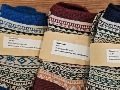 Three pairs of patterned winter socks with labels on a wooden surface
