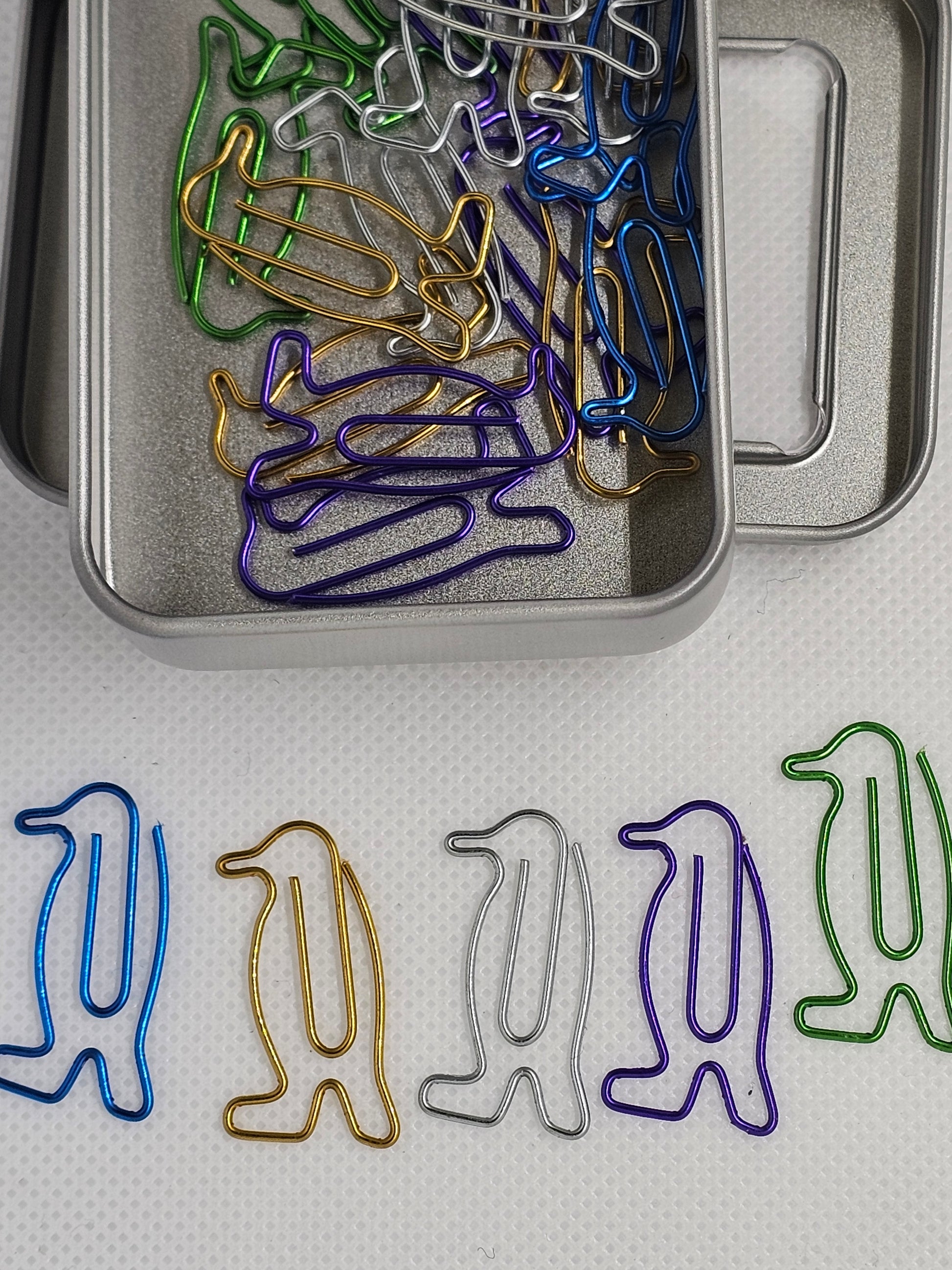 Colorful animal-shaped paper clips in a tin on a textured surface