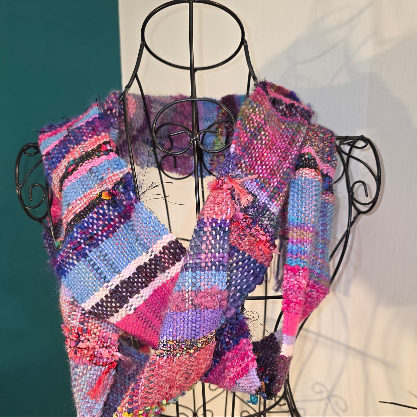 Multicolored knitted scarf on a black wire stand against a white background