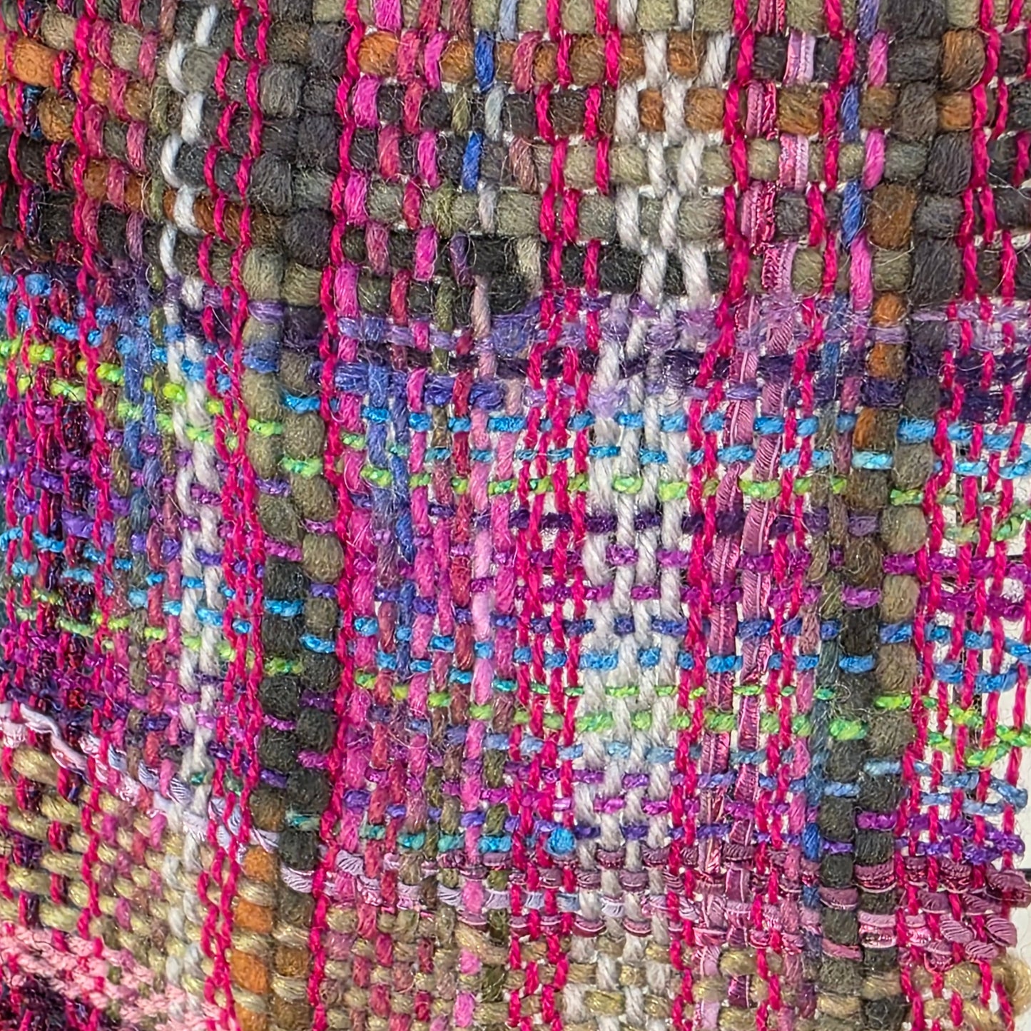 Multicolored woven rug with a pattern of pink, purple, and green on a dark background.