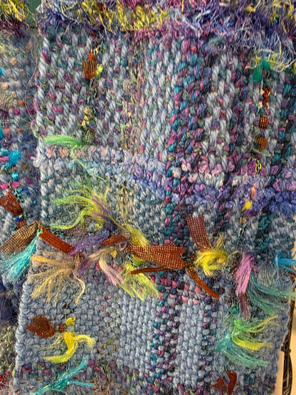 Textile art piece with colorful fibers and a small figure on a textured background