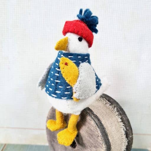 Stuffed toy penguin wearing a red hat and blue sweater on a textured surface.