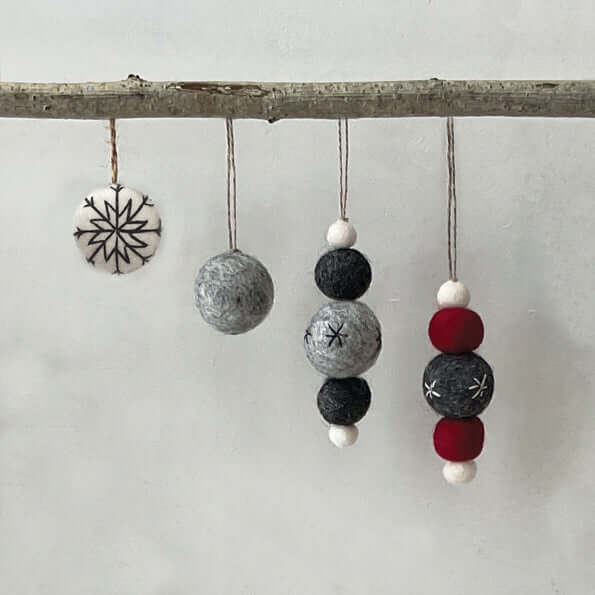 Decorative hanging ornaments with beads and a snowflake design on a branch against a white background.