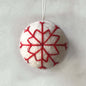 White spherical ornament with red snowflake pattern on a light gray background