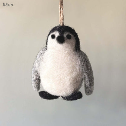 Felted penguin ornament hanging on a string against a neutral background