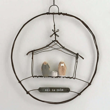 Decorative metal wreath with small figurines, featuring the text 'All is calm' on a white background.