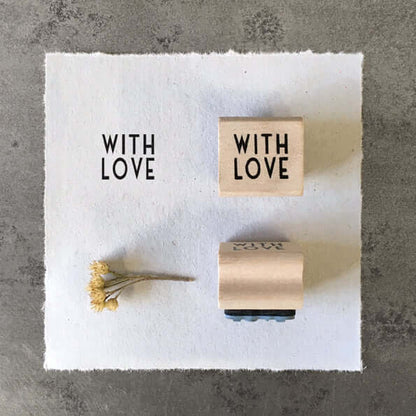 Two wooden stamps with 'WITH LOVE' text on a white paper with a gray background.