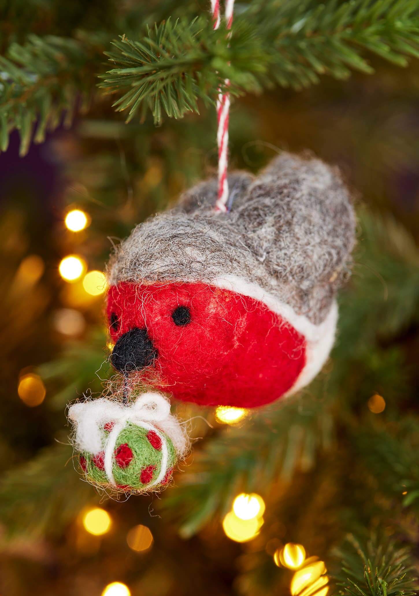 Felted wool robin decoration hanging on a Christmas tree with blurred lights in the background