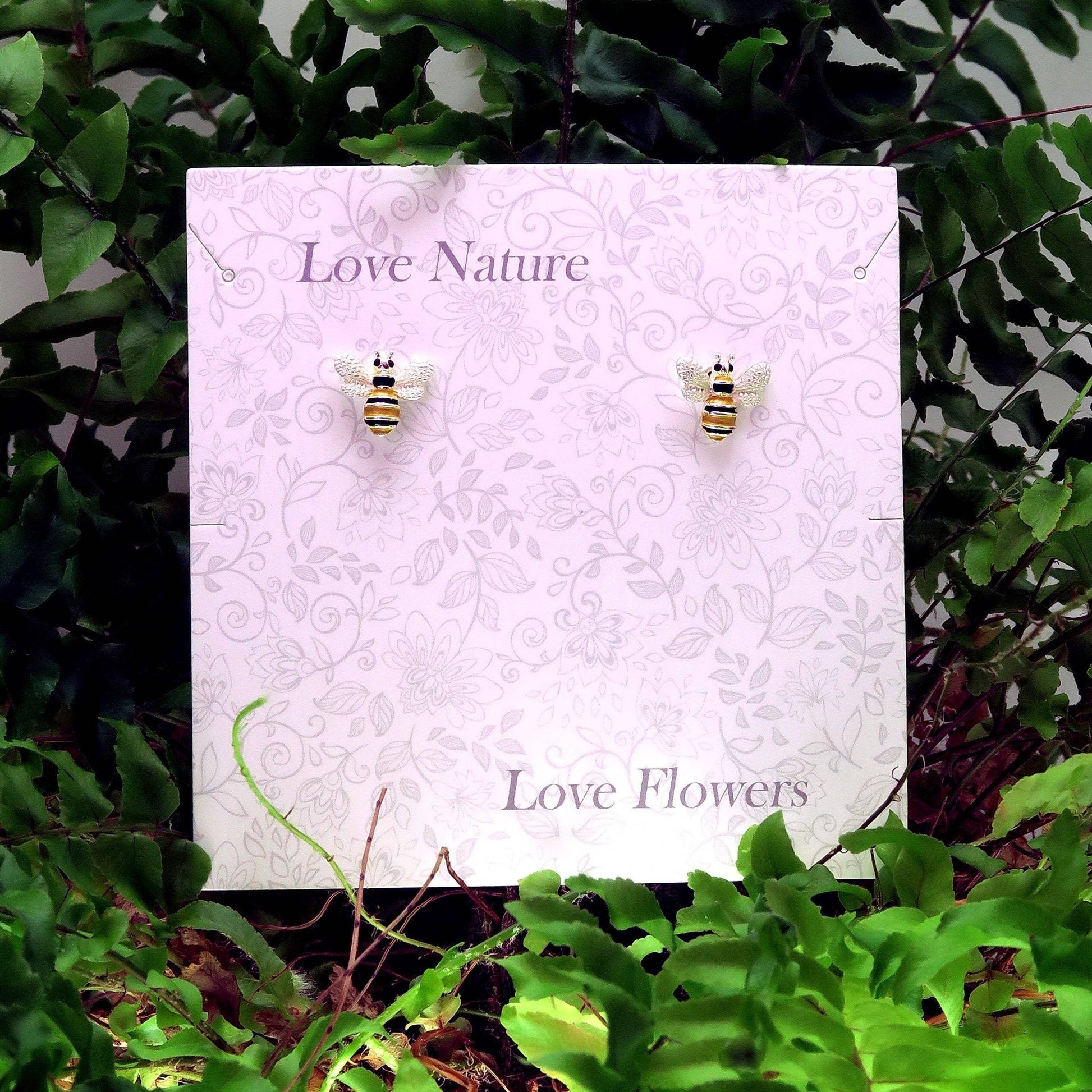 Bee-shaped earrings on a 'Love Nature, Love Flowers' card with green foliage in the background