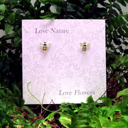 Bee-shaped earrings on a 'Love Nature, Love Flowers' card with green foliage in the background