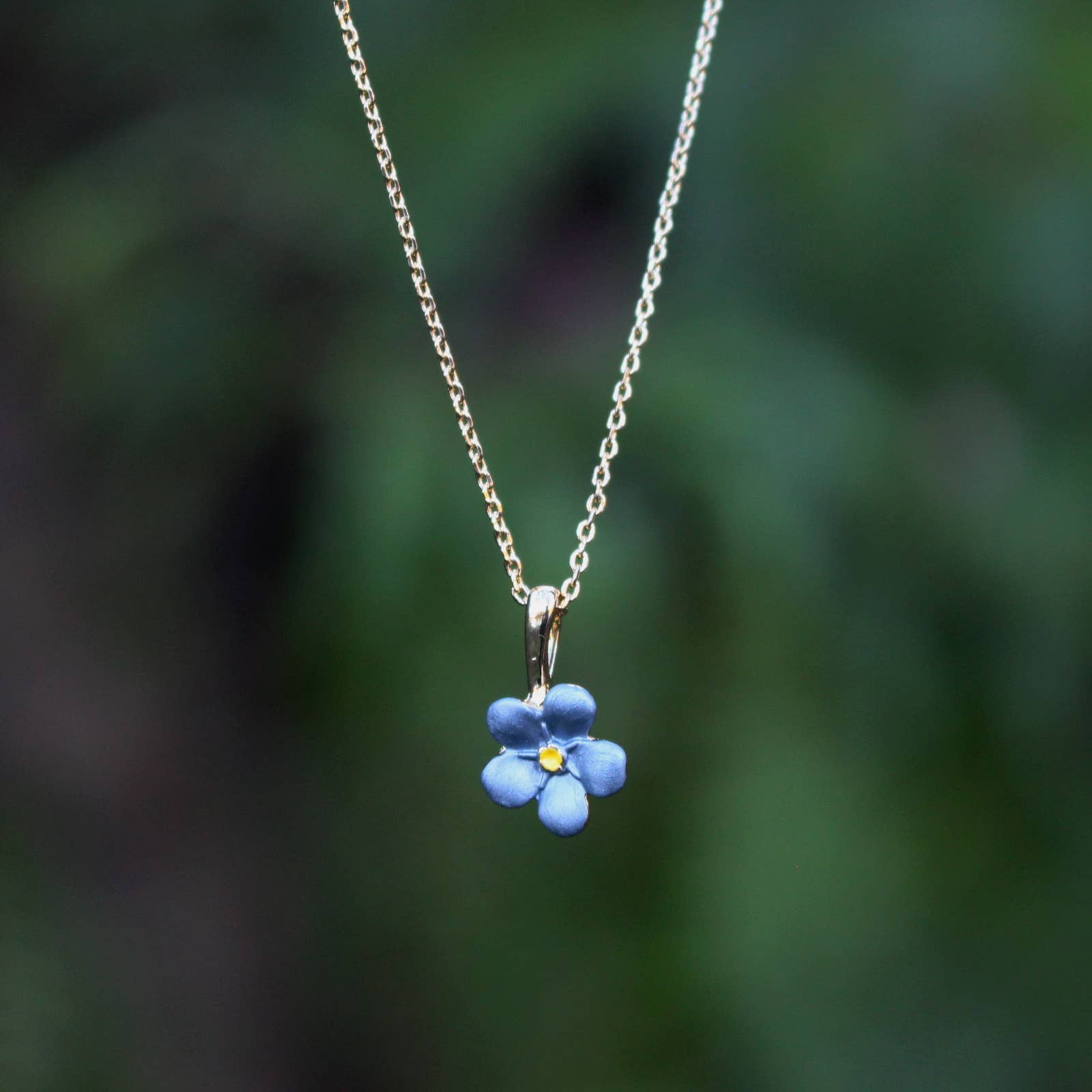 Necklace with a blue flower pendant against a blurred green background