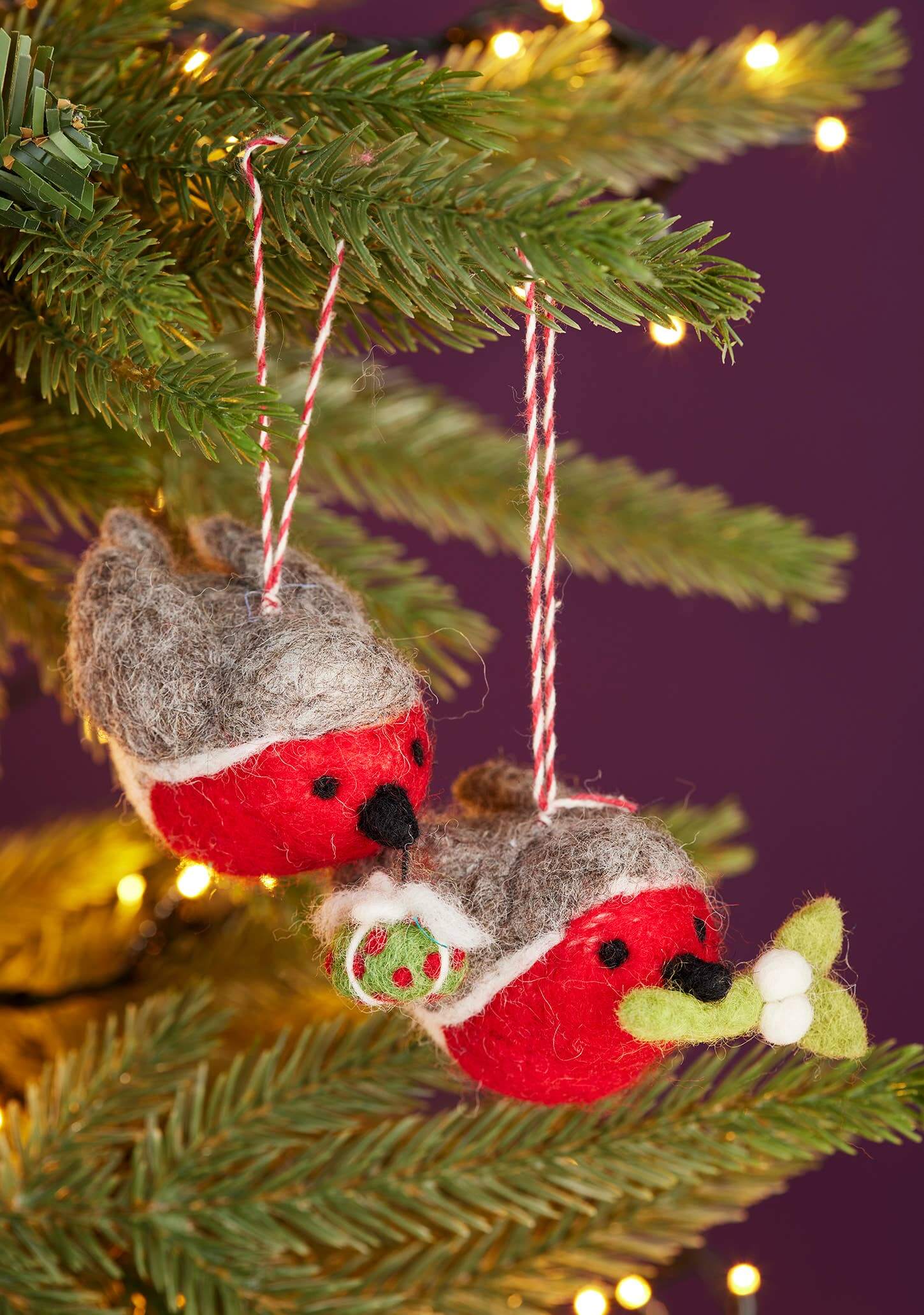 Two red and gray bird-shaped Christmas ornaments hanging on a tree branch with a purple background.