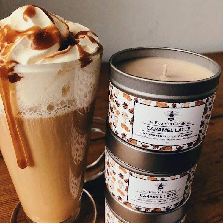 Caramel latte candle next to a glass of caramel latte on a wooden surface