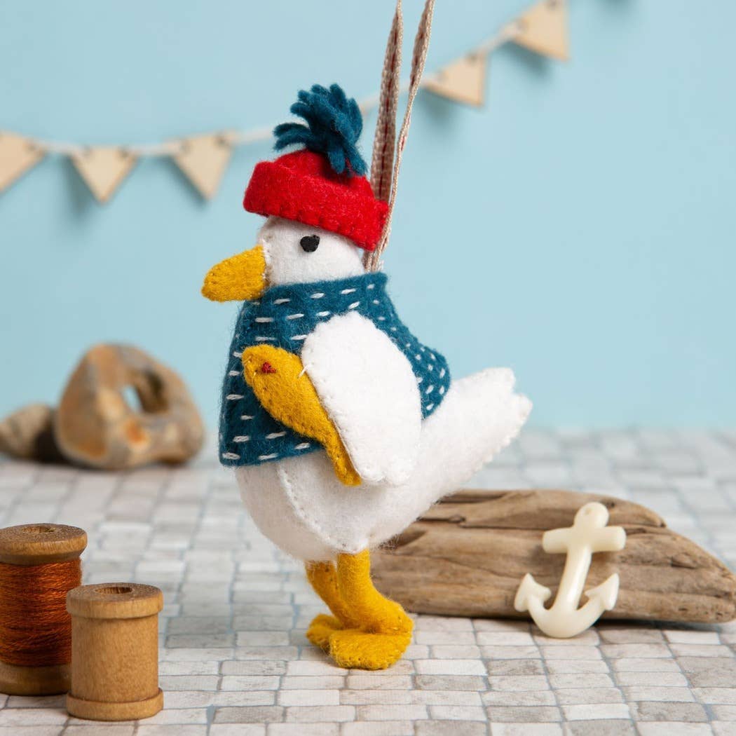 Toy duck wearing a red hat and blue sweater on a textured surface with driftwood and an anchor.