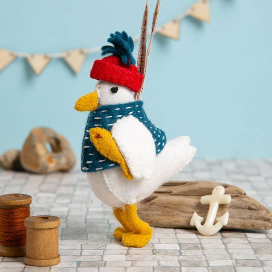 Toy duck wearing a red hat and blue sweater on a textured surface with driftwood and an anchor.