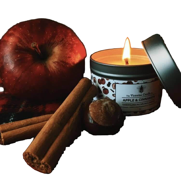 Candle labeled 'Apple & Cinnamon' with an apple, cinnamon sticks, and a nut on a dark surface.
