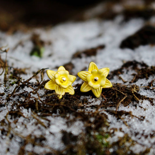 Yellow flower-shaped earrings on a snowy ground with blurred background