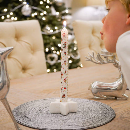 Decorative candle with floral design on a stand in front of a Christmas tree.