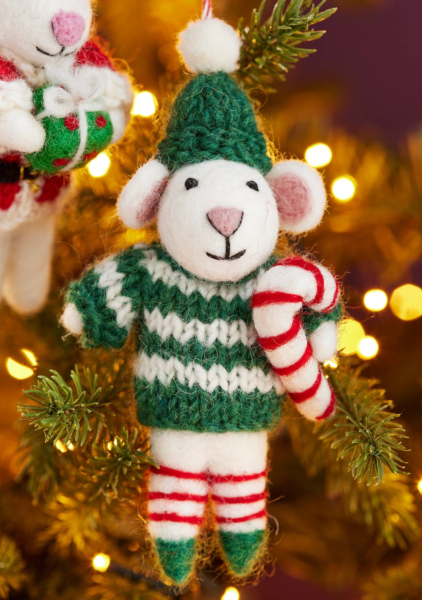 Decorative mouse ornament in a green sweater and striped pants, holding a candy cane, on a Christmas tree.