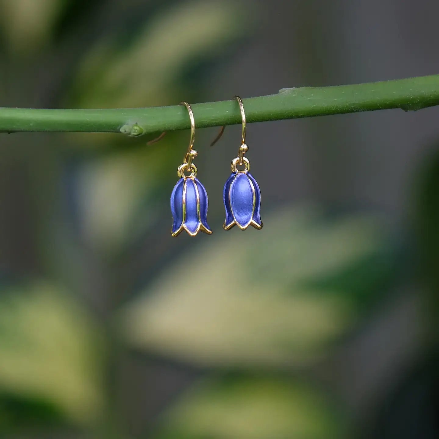 Bluebell-shaped earrings on a green stem with a blurred natural background