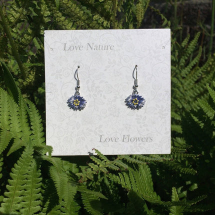 A pair of dangling flower earrings displayed on a white card that reads 'Love Nature' at the top and 'Love Flowers' at the bottom, set against a background of green fern leaves.