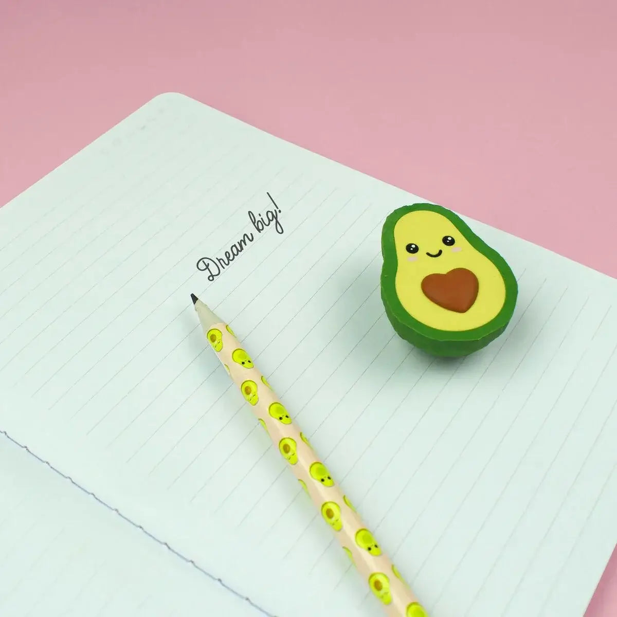 Avocado-shaped eraser on a notebook with a pencil next to it on a pink background