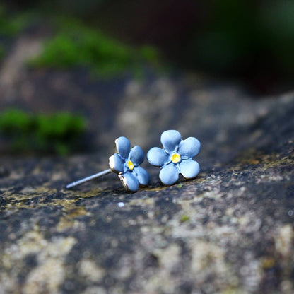 Blue flower-shaped earrings on a textured stone surface