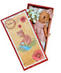 Teddy bear in a decorative box with floral elements on a wooden surface