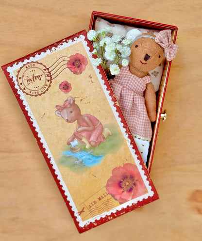 Teddy bear in a decorative box with floral elements on a wooden surface