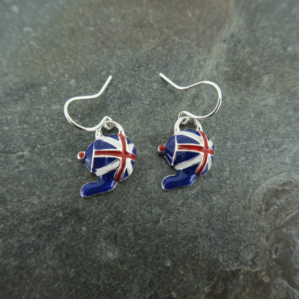 A pair of silver fishhook earrings with small enamel hat charms decorated in a Union Jack pattern, resting on a dark gray slate surface.