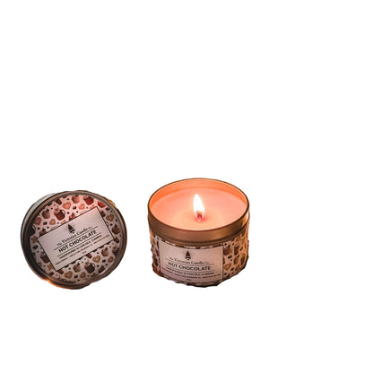 Hot chocolate candle, glass mug with hot chocolate, and book on a soft surface with string lights.