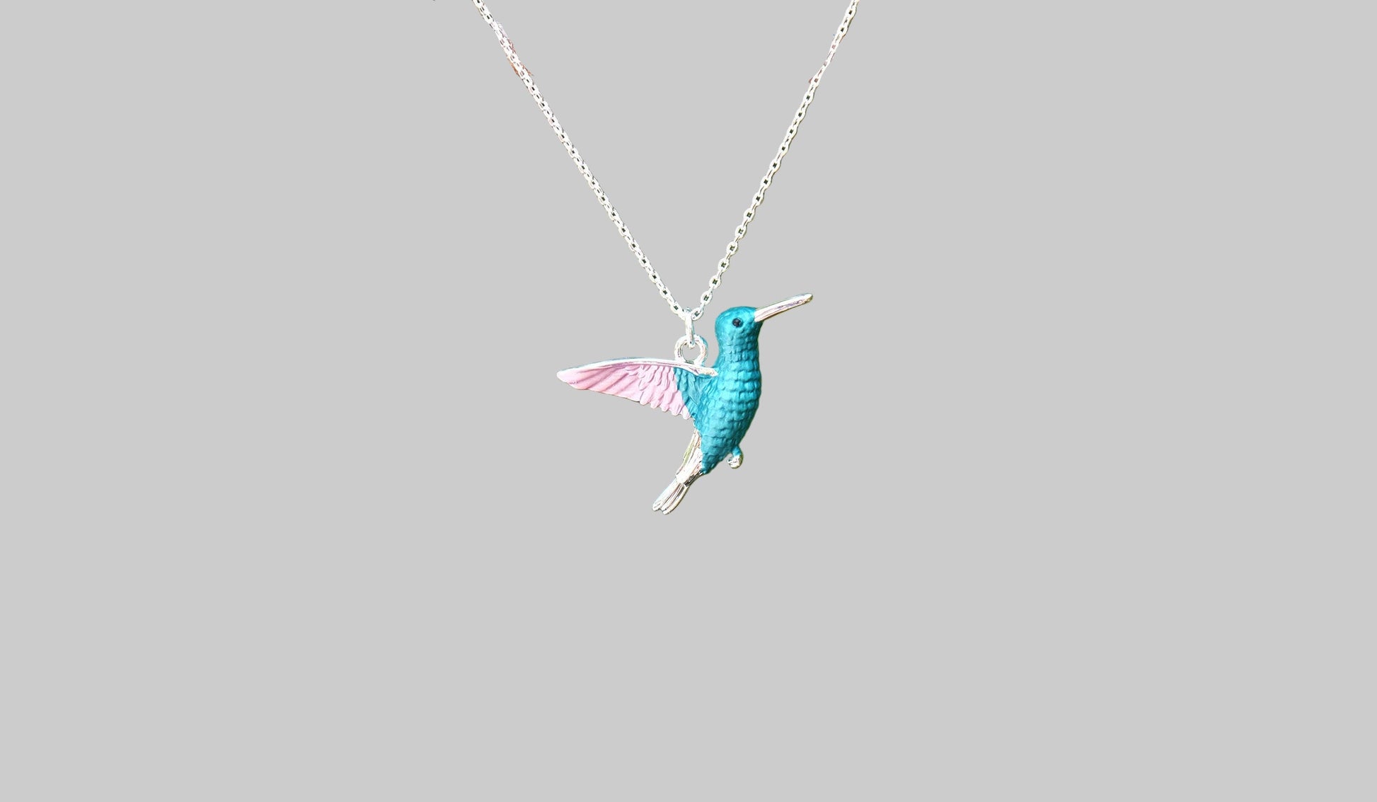Teal hummingbird pendant on a silver chain against a light gray background