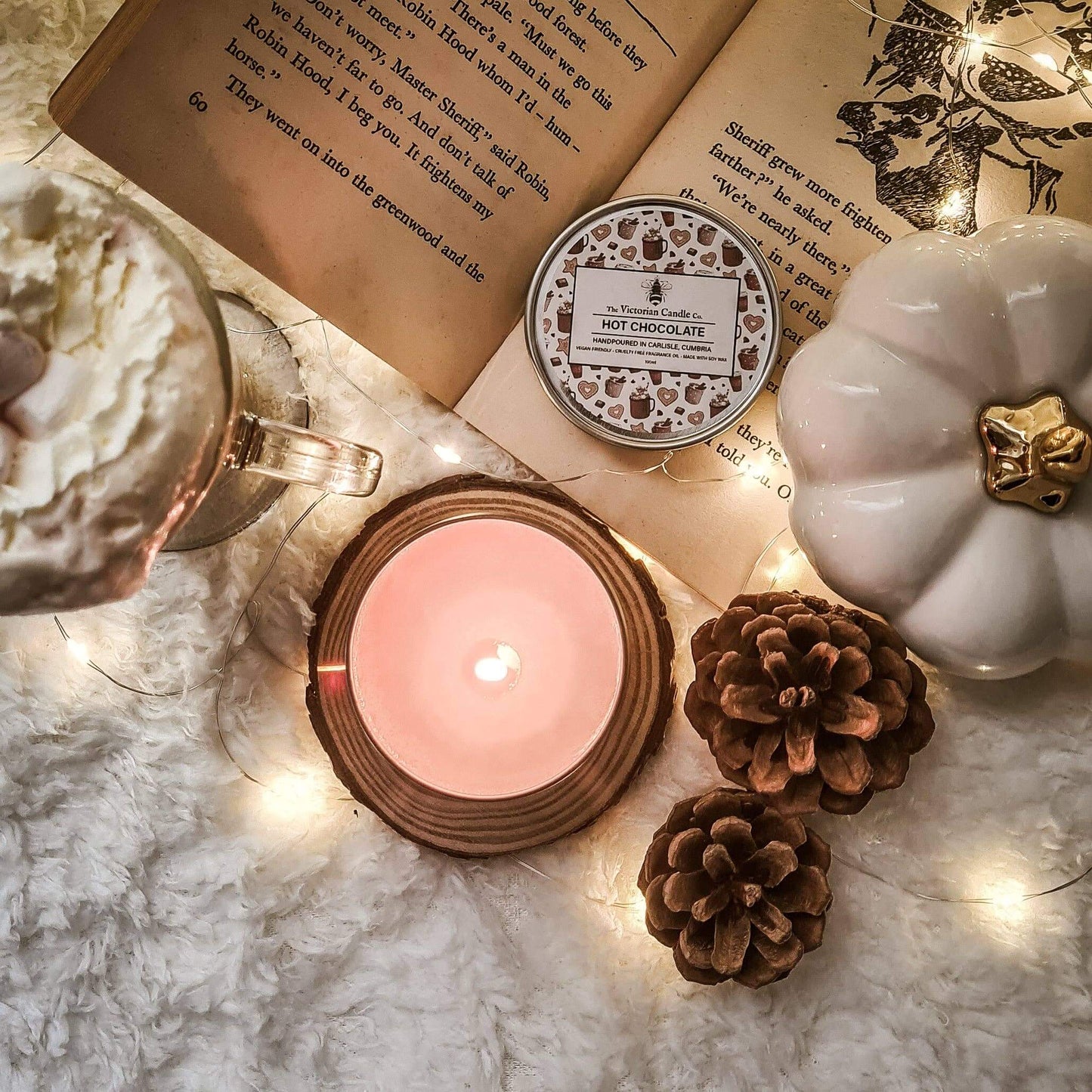 Candle, mug with hot chocolate, and decorative items on a marble surface with string lights.