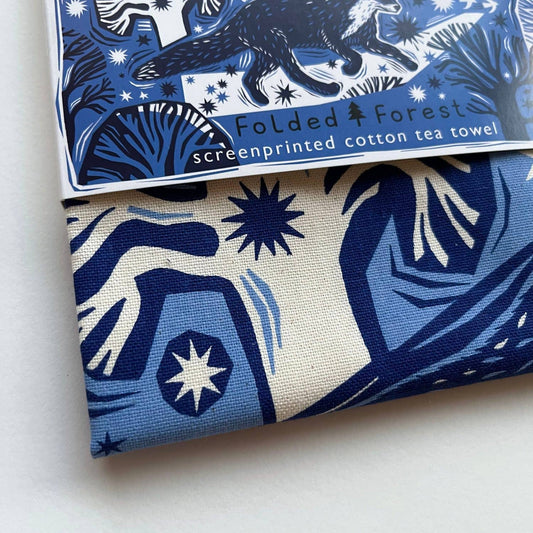 Folded forest-themed screenprinted cotton tea towel with blue and white design.