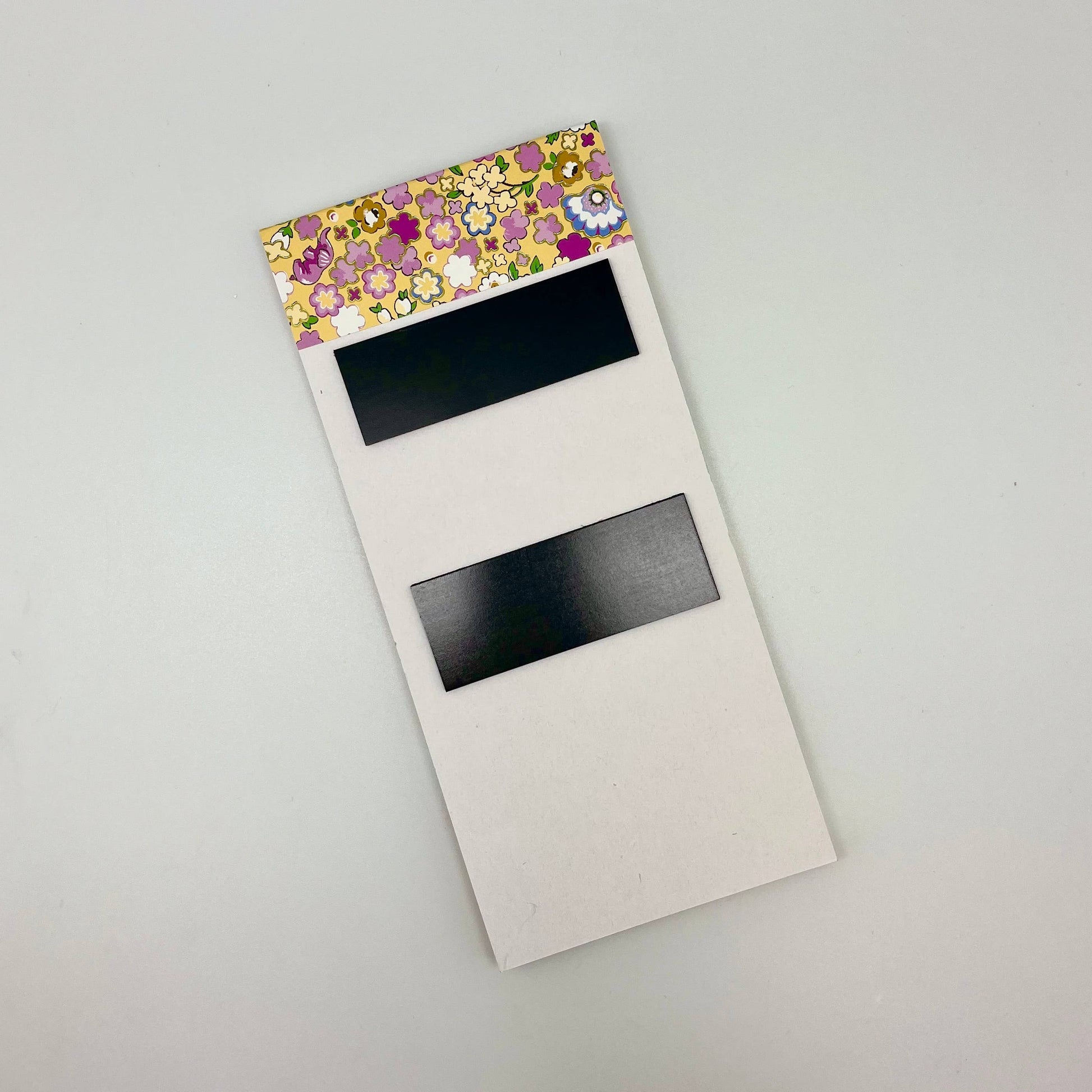 Floral-patterned notepad with black magnetic strips on a light gray background