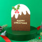 Christmas-themed card with a brown box, white icing, and holly leaves on a green background.