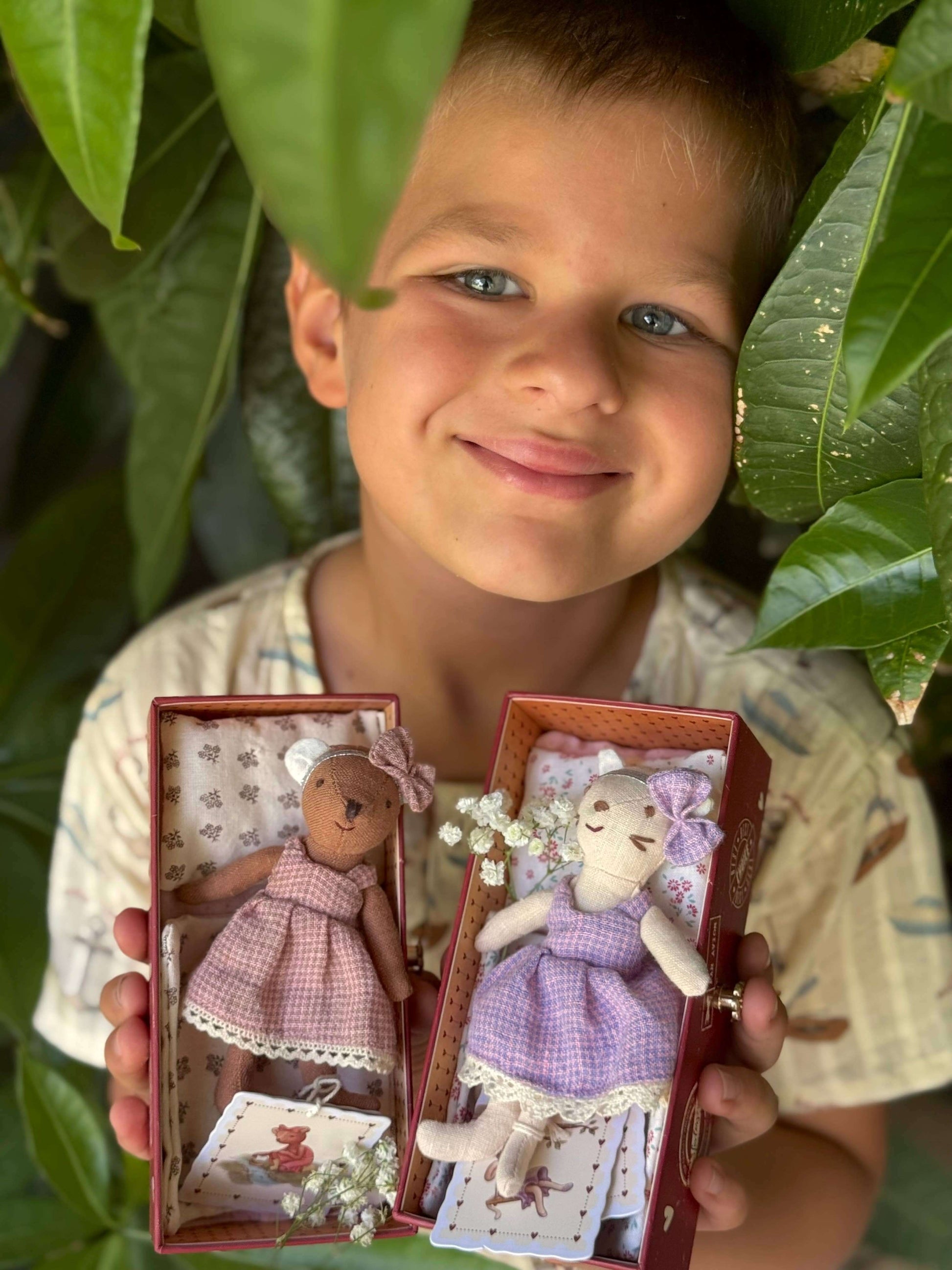 Child holding two teddy bears in boxes with green leaves in the background