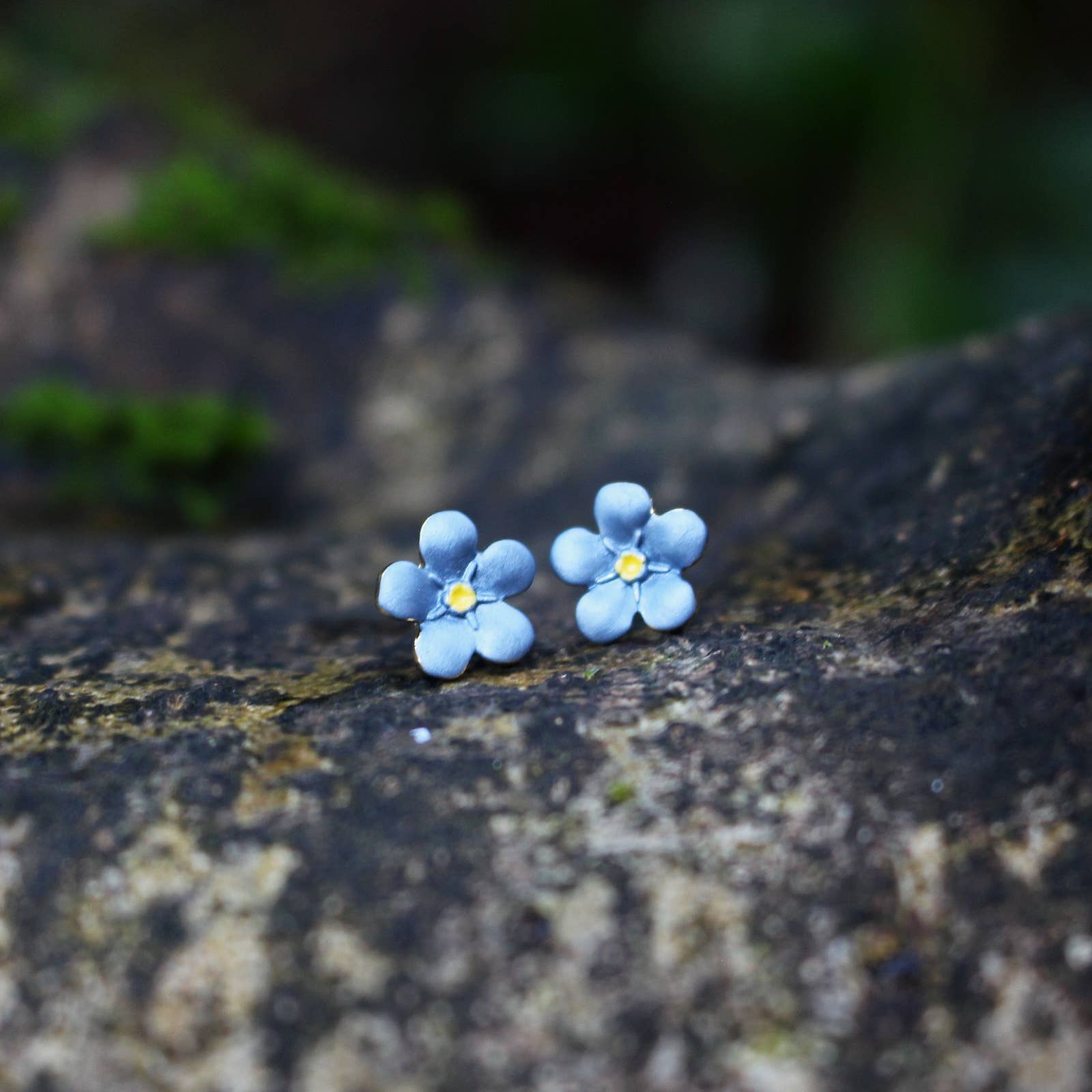 Blue flower-shaped earrings on a textured stone surface