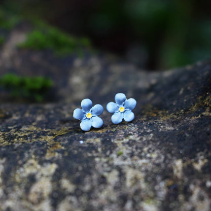 Blue flower-shaped earrings on a textured stone surface