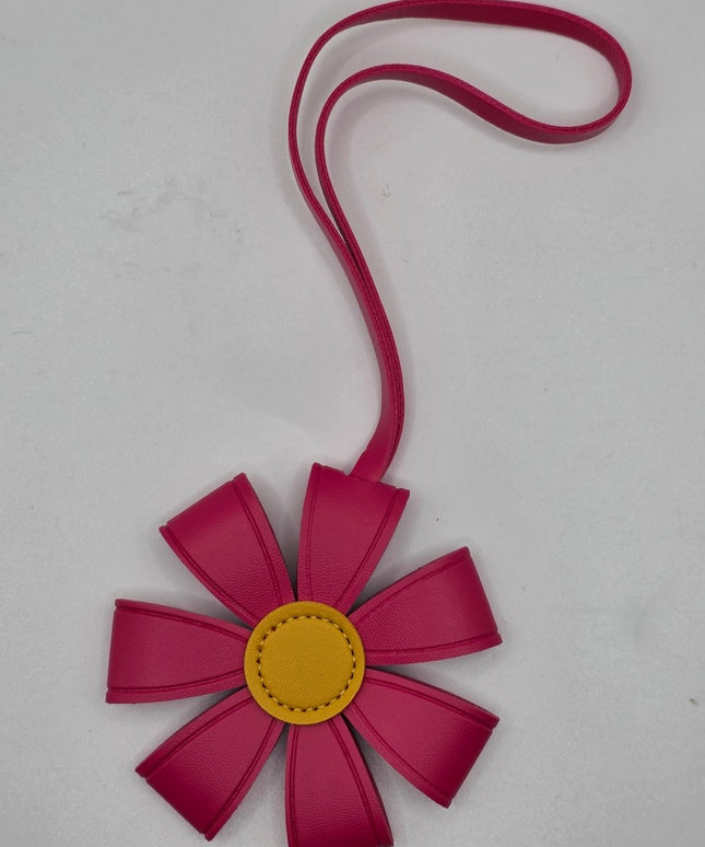 A flower-shaped handbag or pouch in vibrant magenta pink faux leather with a yellow circular center and a matching pink strap, shown on a light gray background.