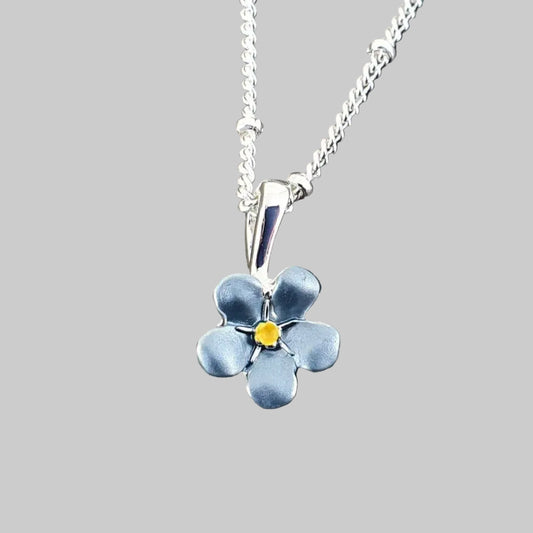 Silver necklace with a blue flower pendant on a gray stone background