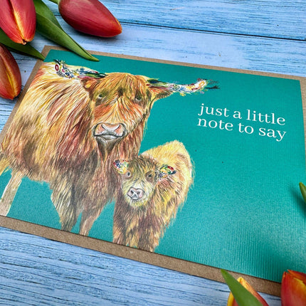 Greeting card with highland cows and tulips on a blue wooden surface