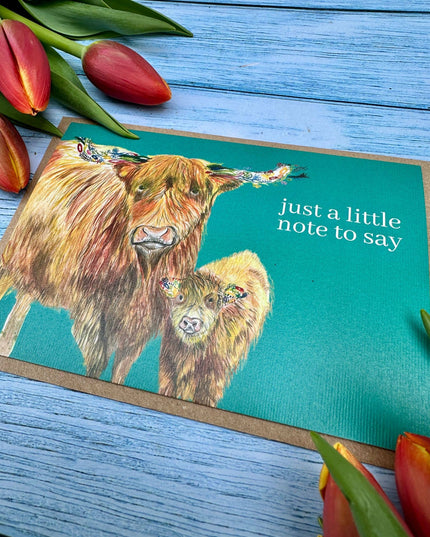 Greeting card with highland cows and tulips on a blue wooden surface