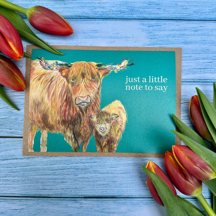 Note card with highland cow illustration and tulips on a blue wooden background