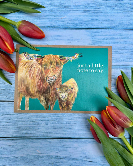 Note card with highland cow illustration and tulips on a blue wooden background