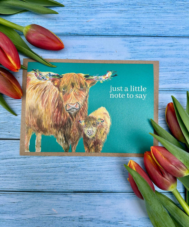 Note card with highland cow illustration and tulips on a blue wooden background