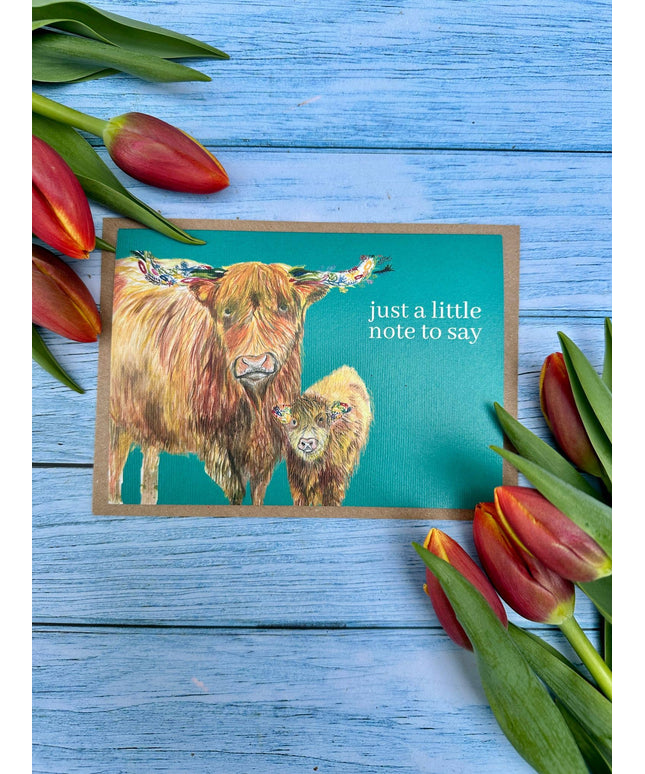 Note card with highland cow illustration and tulips on a blue wooden background