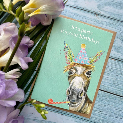 Birthday card with a donkey illustration and flowers on a wooden surface