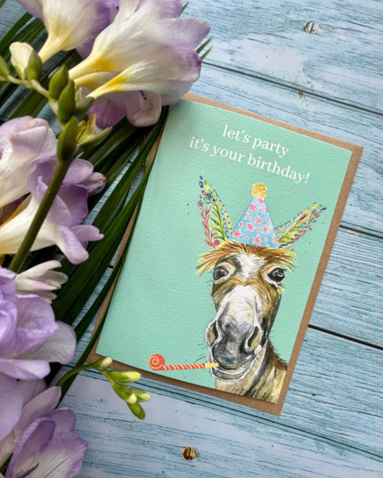 Birthday card with a donkey illustration and flowers on a wooden surface