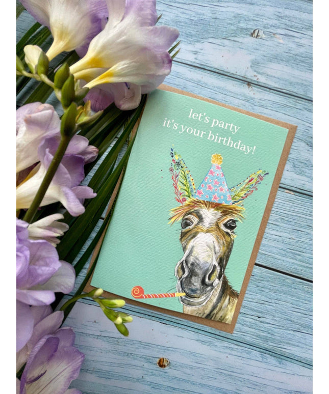 Birthday card with a donkey illustration and flowers on a wooden surface
